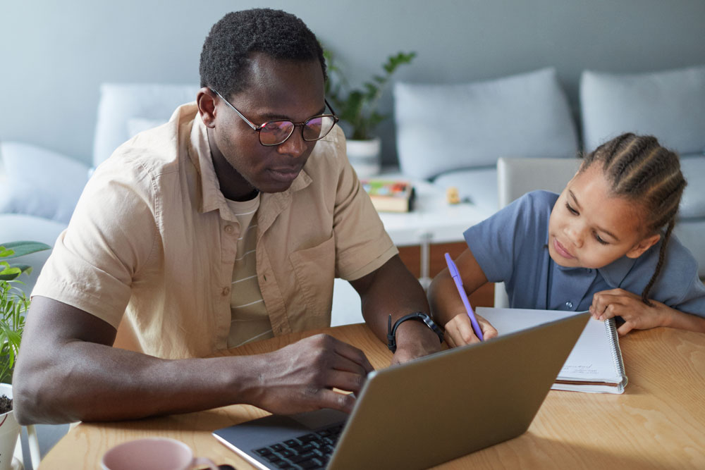 Adult student working on laptop at table with son