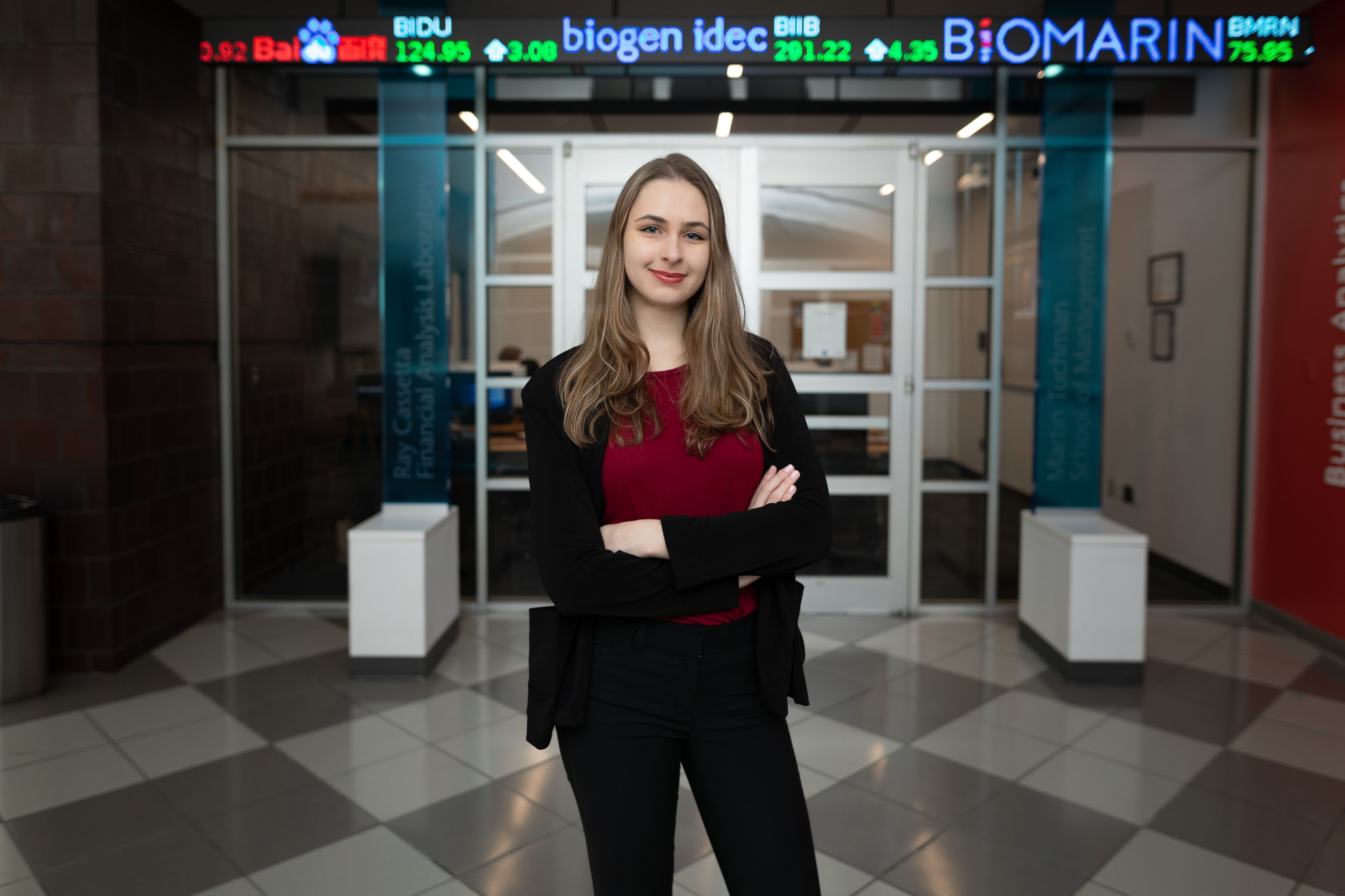 Young female adult business student standing in front of a stocks chart with her arms crossed