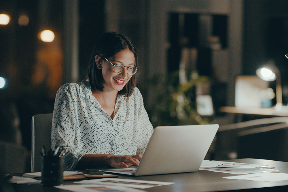 Online adult student smiles while typing on laptop in a home office setting.