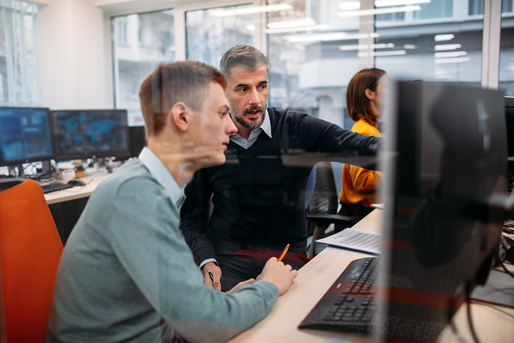 Two cybersecurity professionals reviewing information on a computer screen in an office setting