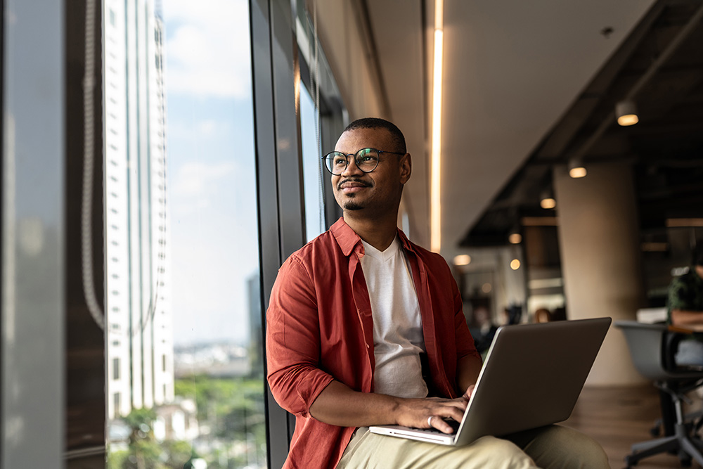 Person sitting in an office with laptop on their lap and looking out the window.