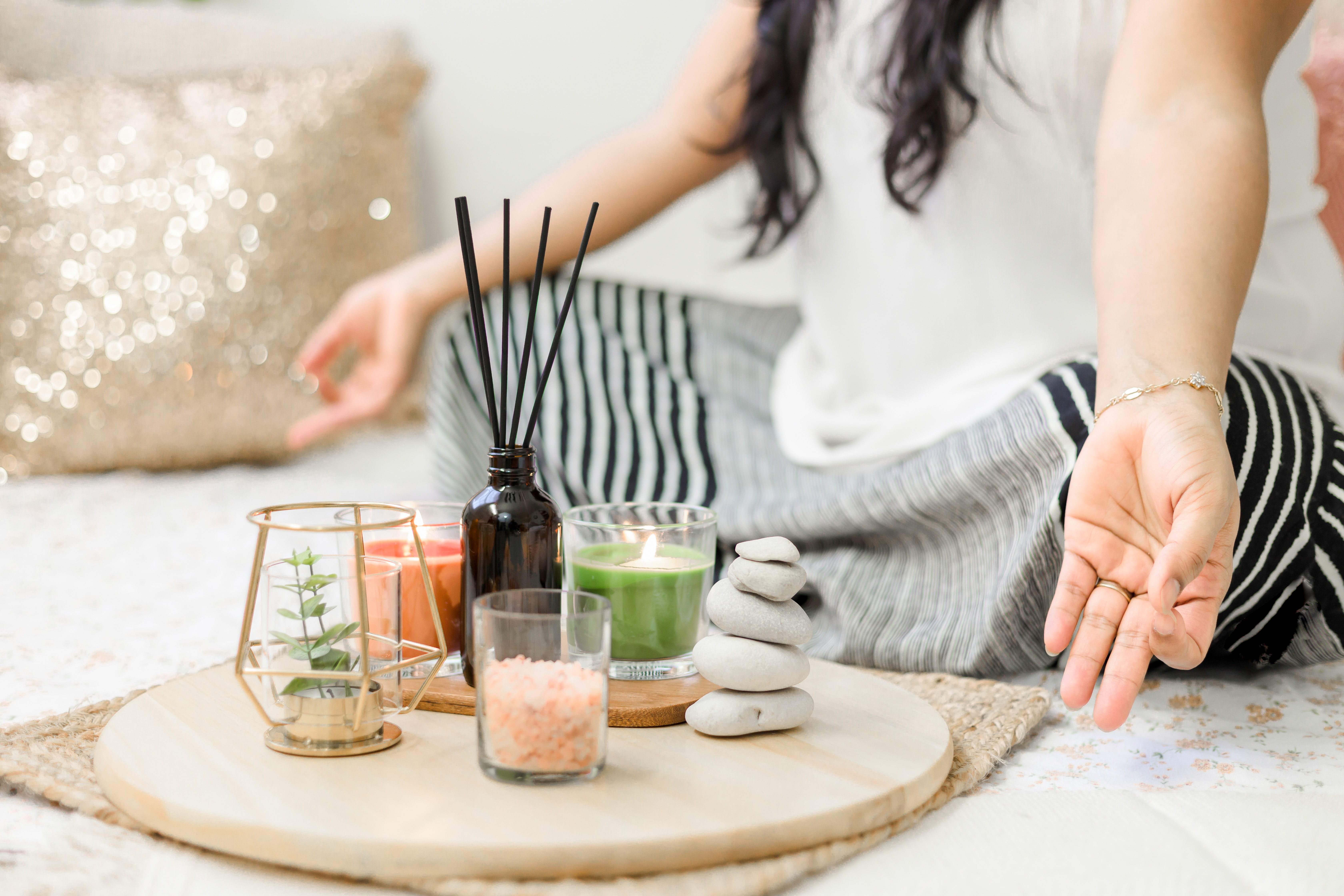 Woman sitting in a meditation position on the ground with candles, incense, and healing stones