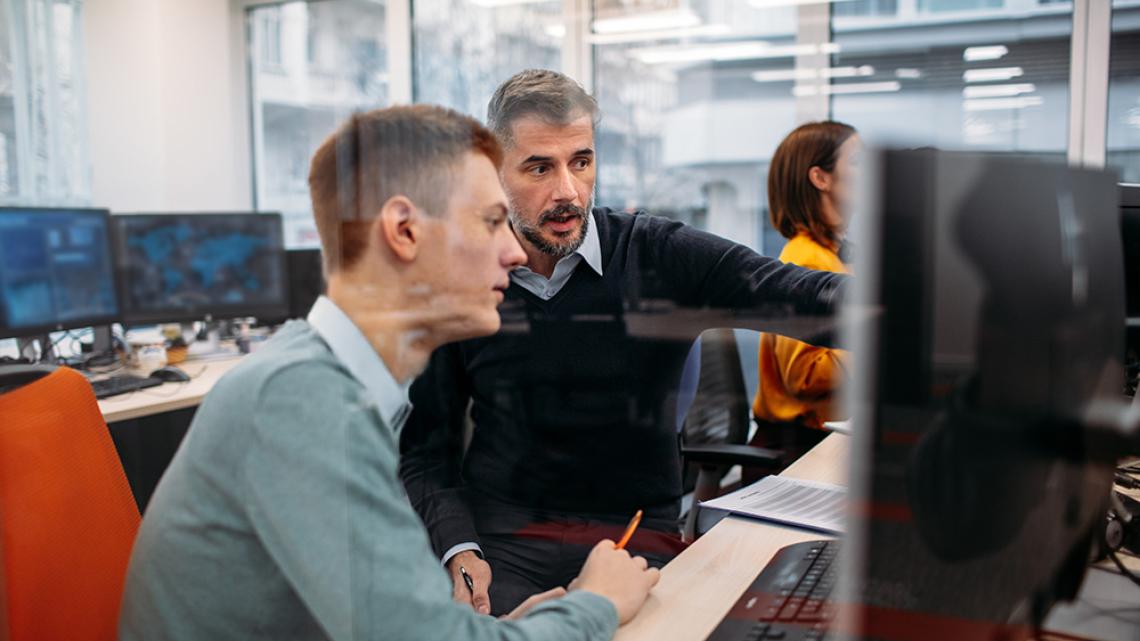 Two cybersecurity professionals reviewing information on a computer screen in an office setting