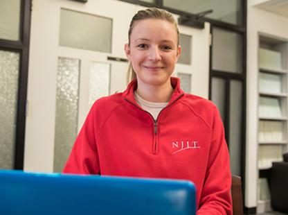 NJIT student smiling with computer in front of them