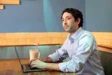 Business student sitting in a cafe doing course work on his laptop