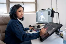 female design student sitting at a desk with her laptop and design pad creating a digital animation with a stylus