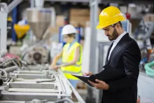 Professional engineer standing in a factory, wearing a hard hat, and taking notes