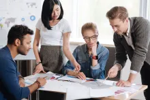 A diverse group of male and female graduate professionals sitting around a table, working together on a project
